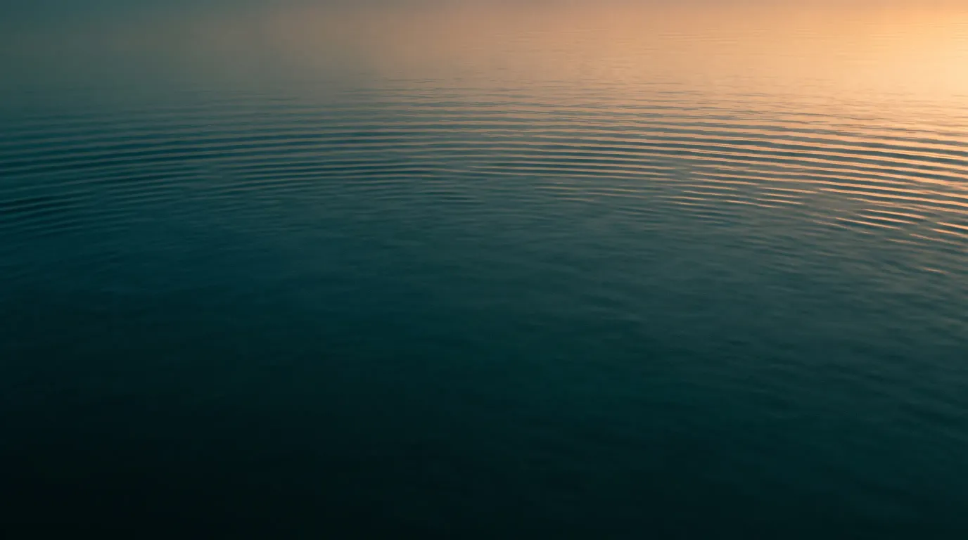 Sanfte Abendwellen auf dunklem Wasser, in denen sich ein schmaler warmer Lichtstreifen spiegelt.