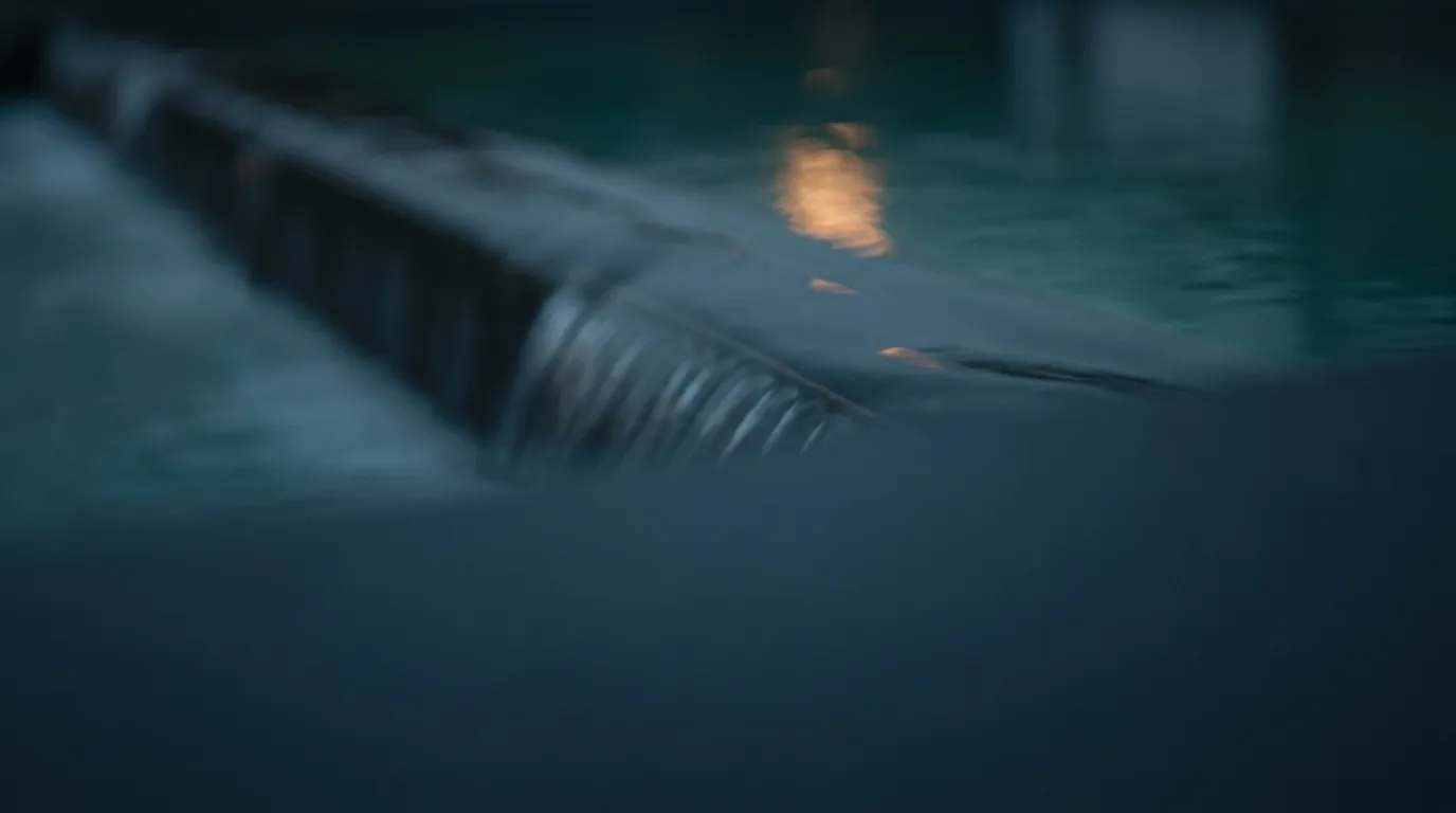 Ein dünner, glatter Wasserfilm fließt gleichmäßig über eine klare Kante ins Dunkle.