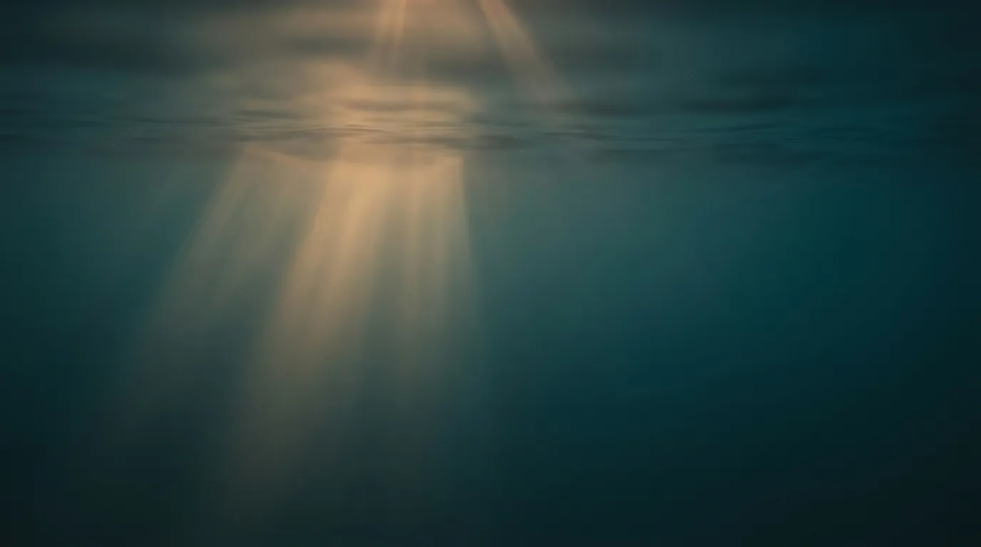Weiche Lichtstrahlen brechen von oben durch eine ruhige Wasseroberfläche.